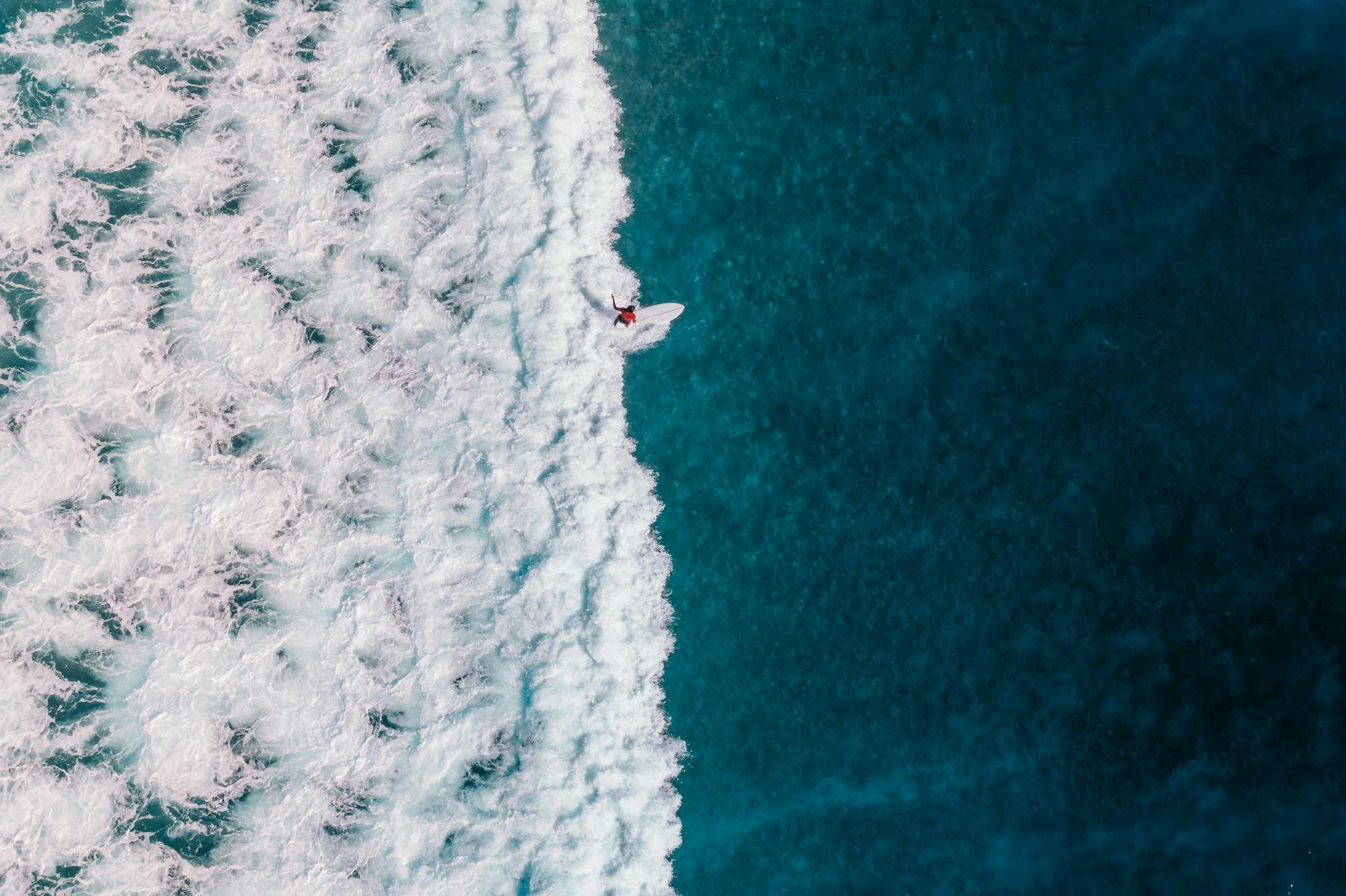 Drone shot capturing a surfer navigating the ocean's waves, showcasing the thrill of watersports.