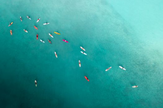 Top-down drone shot of surfers on turquoise sea, showcasing leisure and water sports.