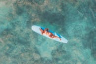 空中拍摄的女人躺在清澈的海水中的冲浪板上，散发出放松和休闲的感觉