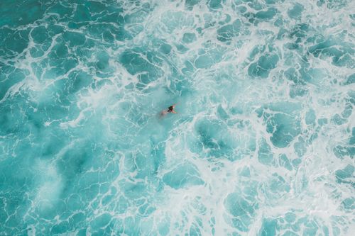 Free Relaxing aerial view of a swimmer in turquoise ocean waves, capturing serenity and freedom. Stock Photo