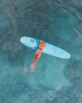 Woman in bikini floating on surfboard in clear blue water, showcasing a moment of summer relaxation.