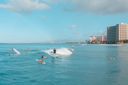 Surfers ride waves on a sunny day at Waikiki Beach with a view of the Honolulu skyline in the background.