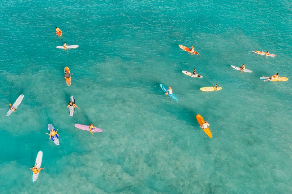 A vibrant aerial shot capturing surfers on colorful boards in turquoise ocean waters.