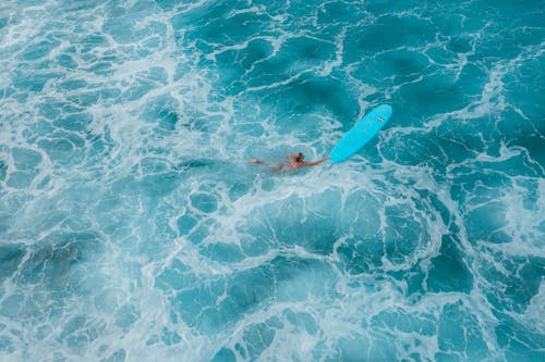 Aerial View of a Woman Swimming to Her Surfboard in Foamy Water 