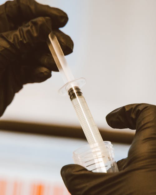 Close-up of Person in Rubber Gloves Holding a Tube and a Syringe 