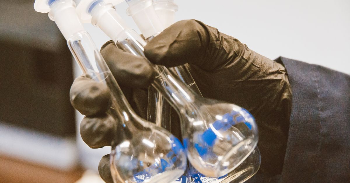 Lab technician holding a flask of cultured fat with a bioreactor in the background