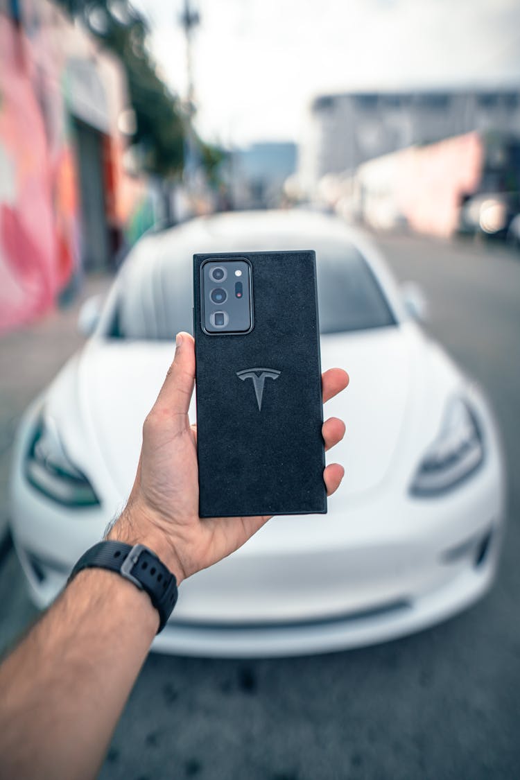 A Person Holding A Smart Phone In Front Of A Car