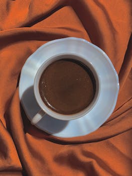 A close-up of an espresso cup set on rich, orange fabric, creating a warm, inviting still life.