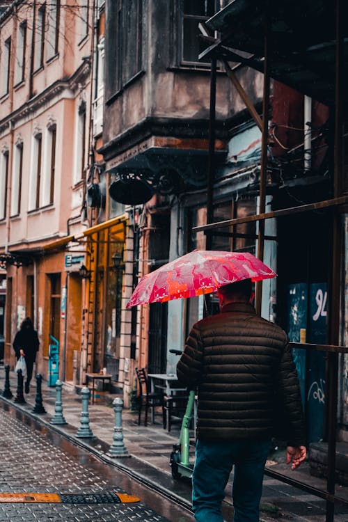 Back View of a Man Walking while Holding a Pink Umbrella