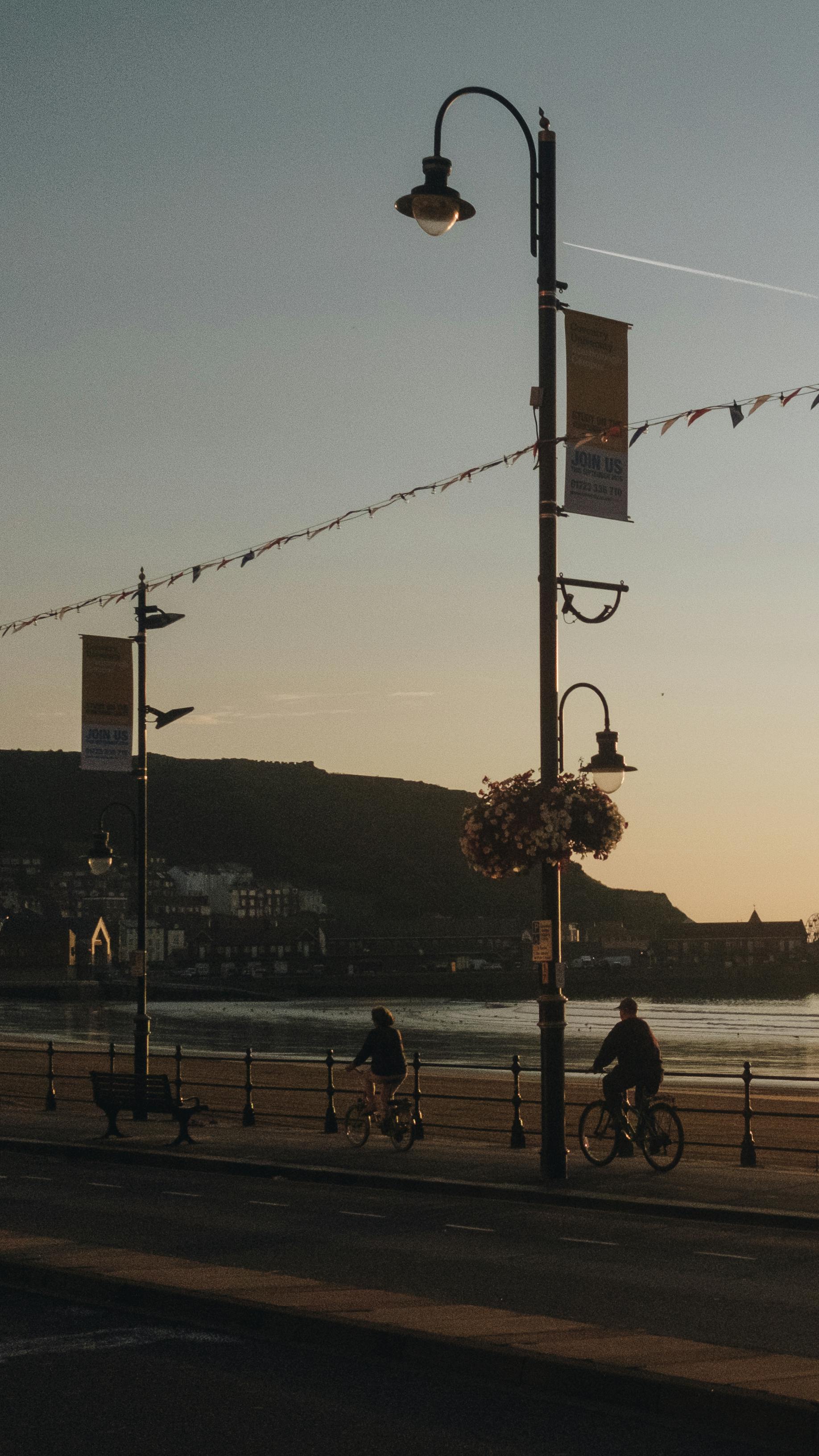 Cyclists enjoy a peaceful ride along a waterfront promenade at sunset, capturing a serene evening scene.