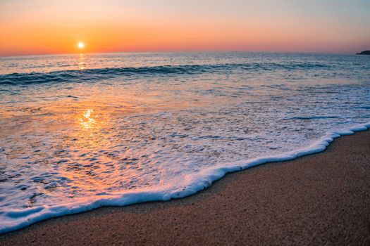 Serene beach at sunset with gentle waves and sun reflection.