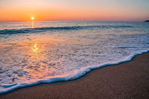 Free Serene beach at sunset with gentle waves and sun reflection. Stock Photo