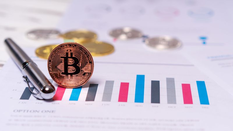 Close-up of a Bitcoin coin placed on financial charts with a pen, symbolizing cryptocurrency and economic analysis.