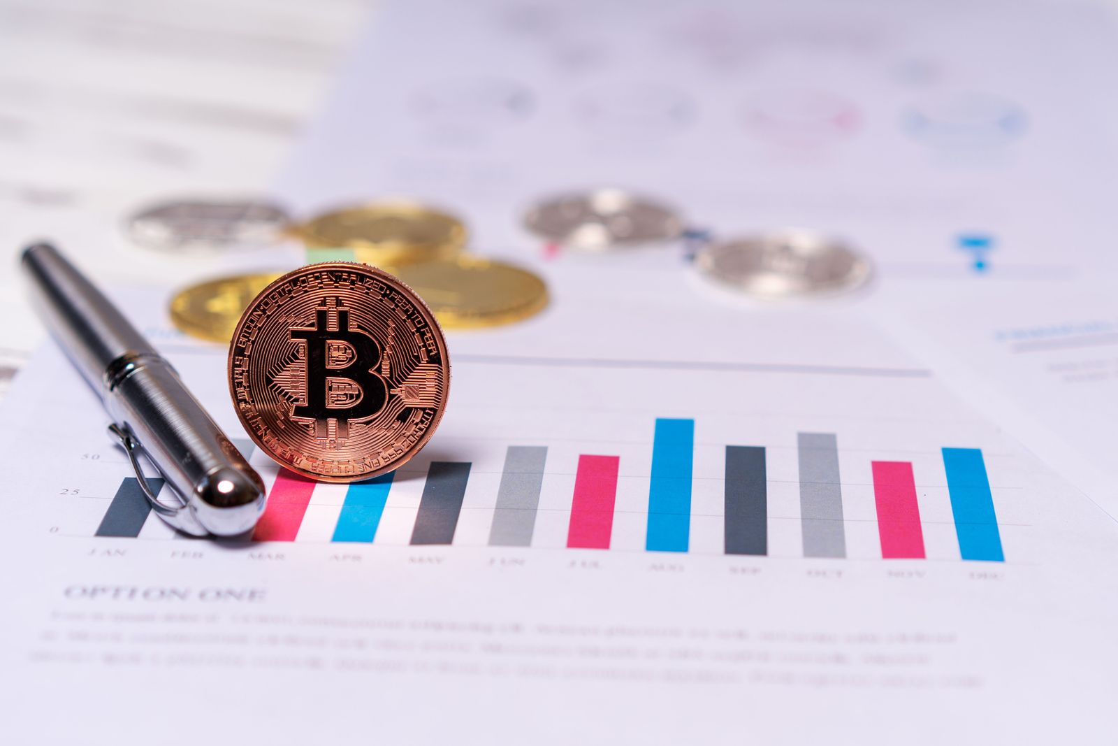 Close-up of a Bitcoin coin placed on financial charts with a pen, symbolizing cryptocurrency and economic analysis.