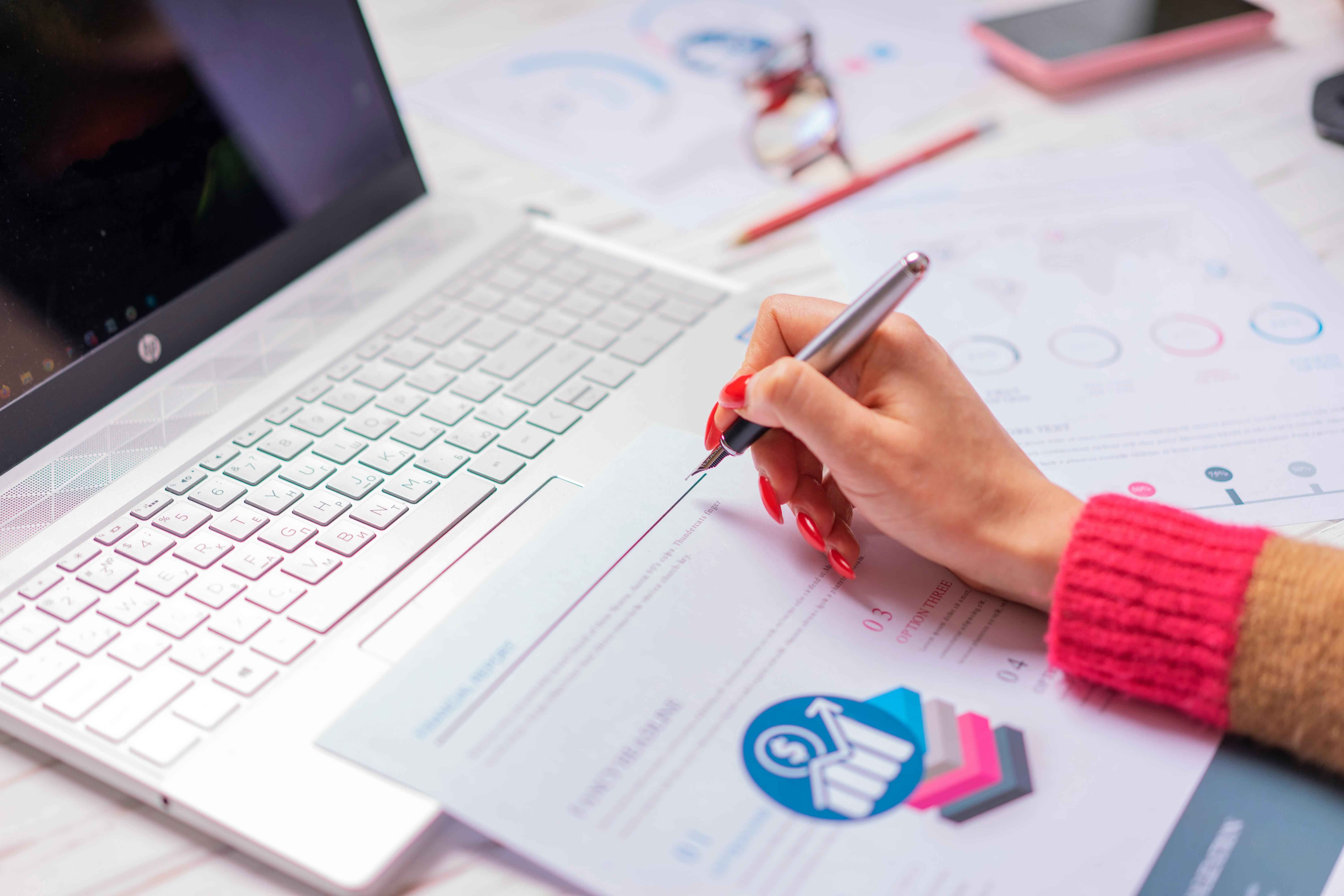 A person analyzes financial data and diagrams on a laptop and paper at a desk, highlighting office work.