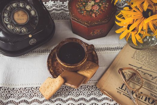 Charming vintage setup with coffee, cookies, retro phone, and flowers on lace.