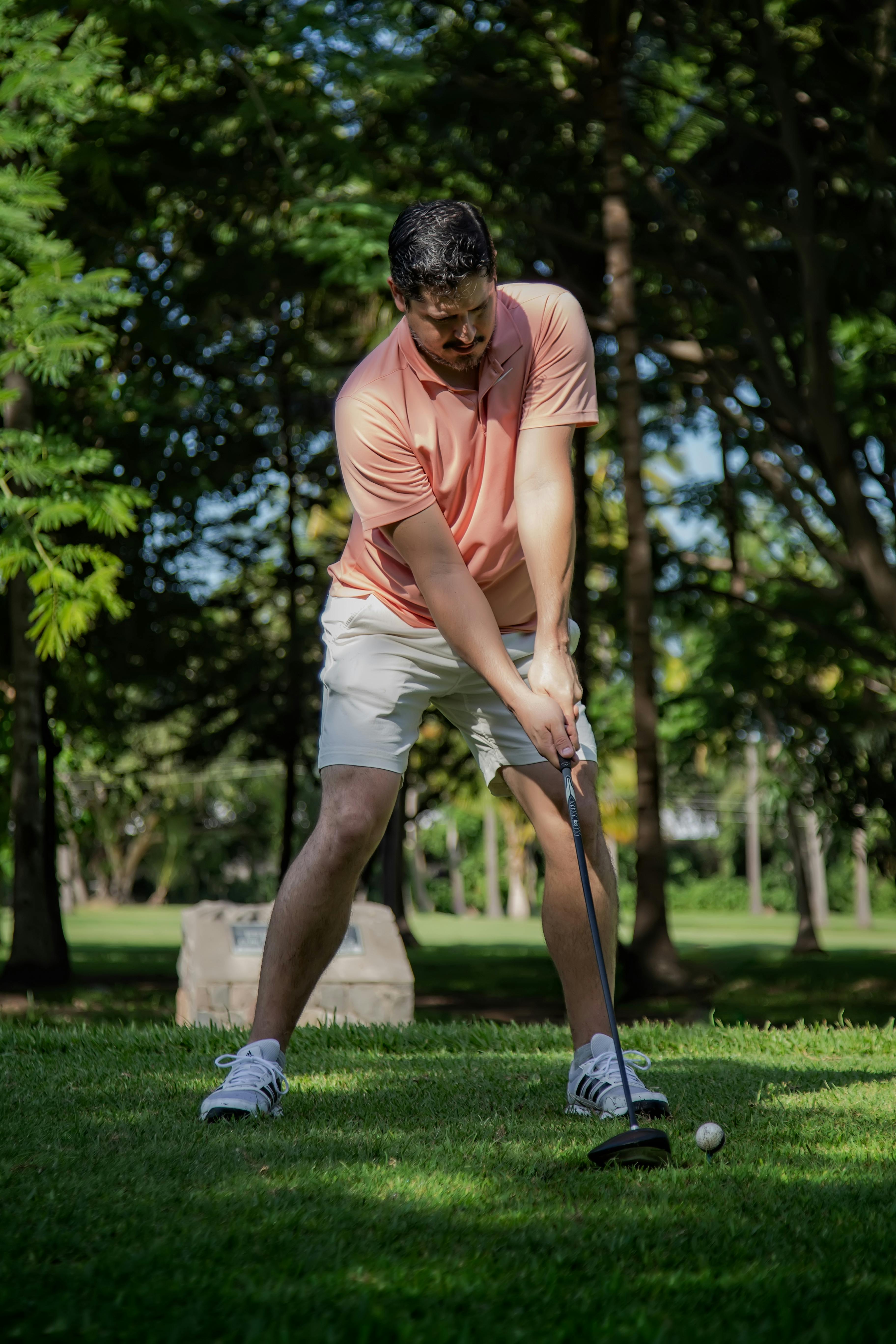 A man in a pink shirt prepares to swing his golf club on a sunny golf course.