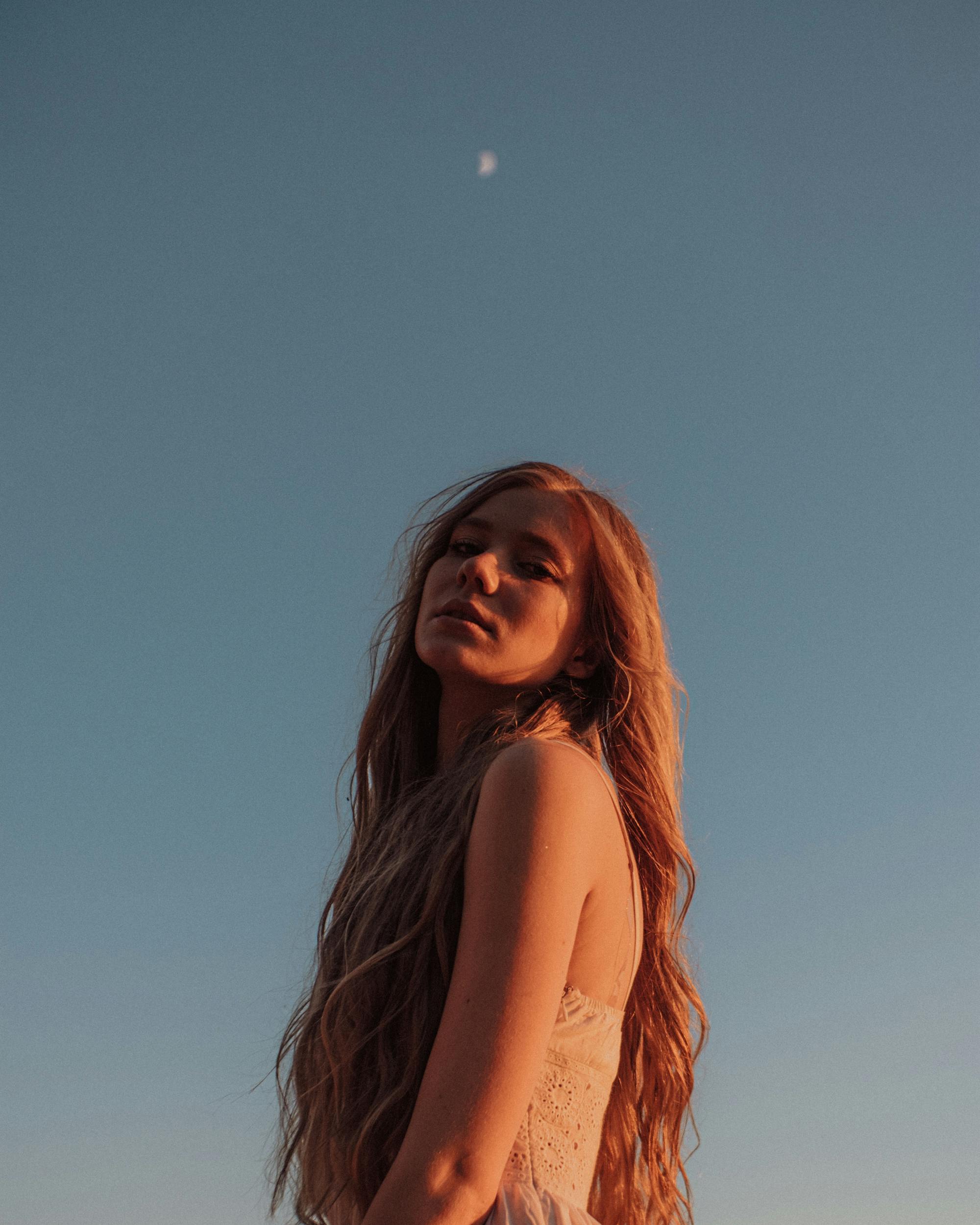 美丽的女人在黄昏时长着红色的头发，对着晴朗的天空，捕捉户外的宁静时刻