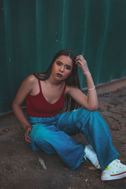 Free Fashionable woman in denim jeans posing outside against a teal backdrop in Ouro Preto, Brazil. Stock Photo