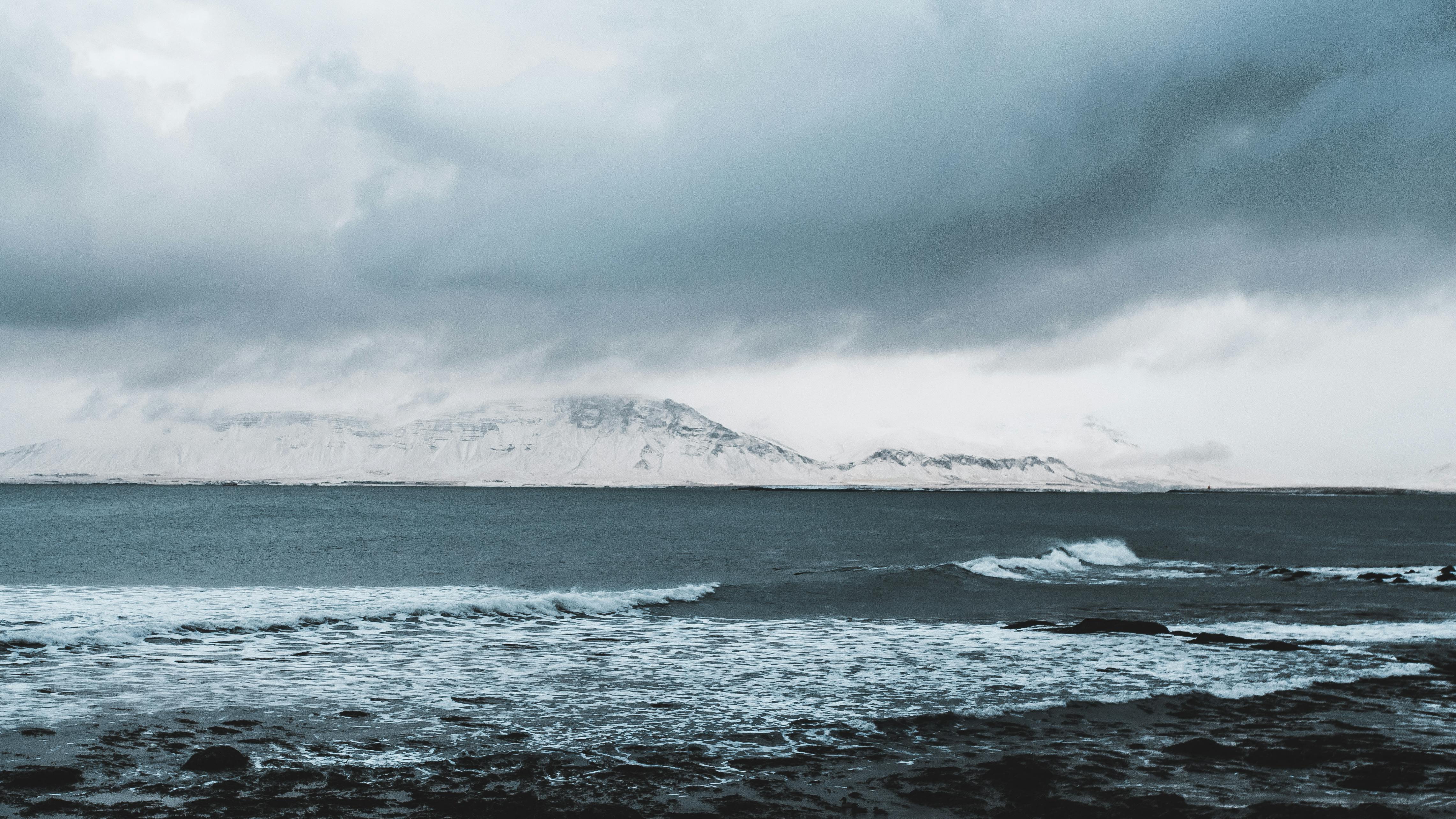 Prescription Goggle Inserts - Serene winter coastal view with snow-covered mountains and a dramatic cloudy sky.