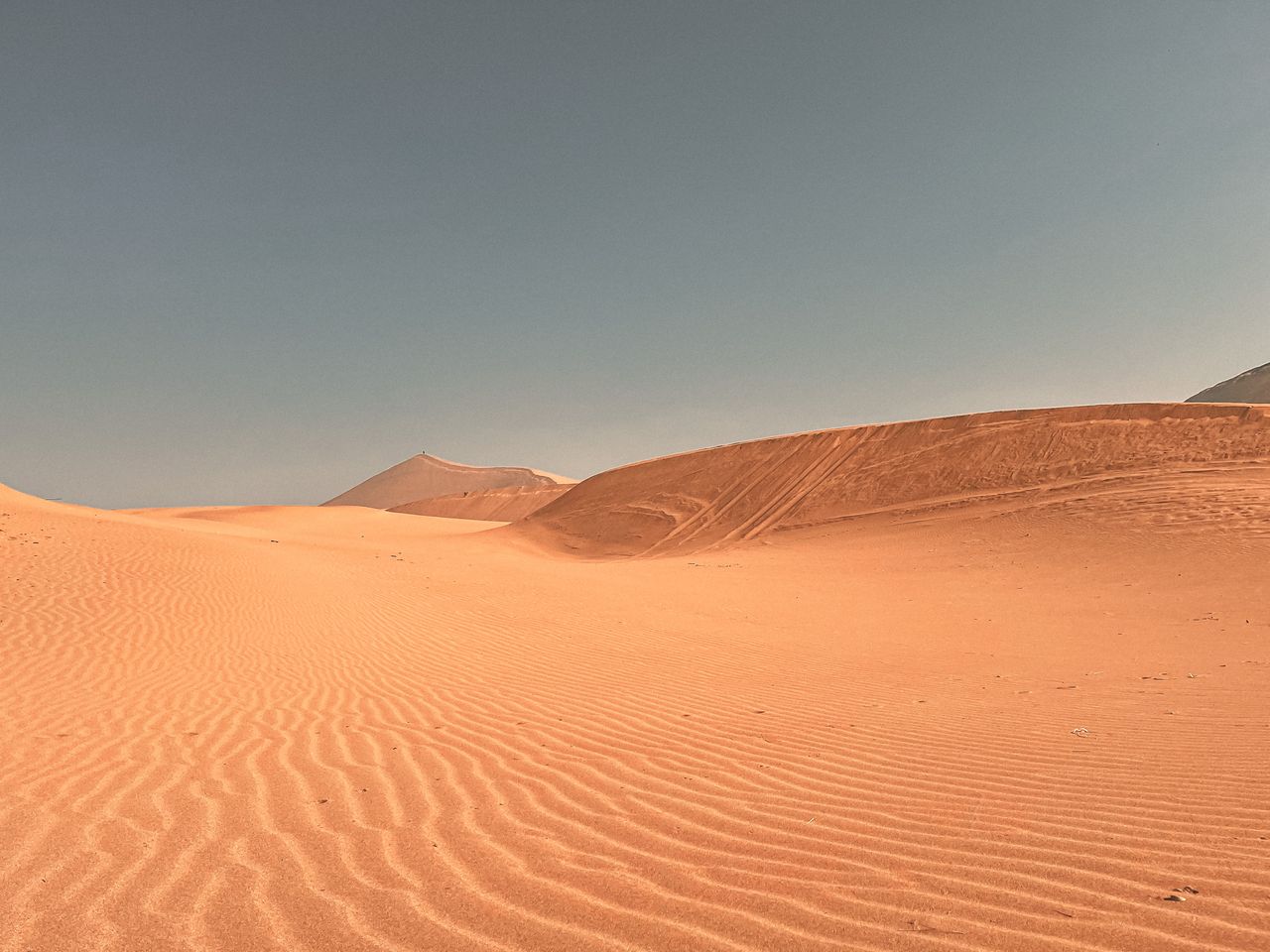 a vast and dry desert with rippled sand dunes under a clear blue sky