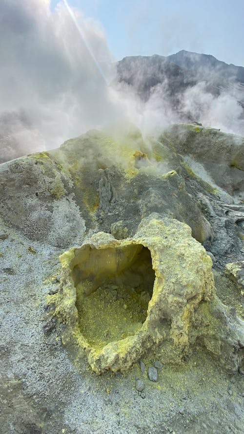 Breathtaking volcanic formation with heavy smoke emitting from geyser under blue sunny cloudless sky in daylight