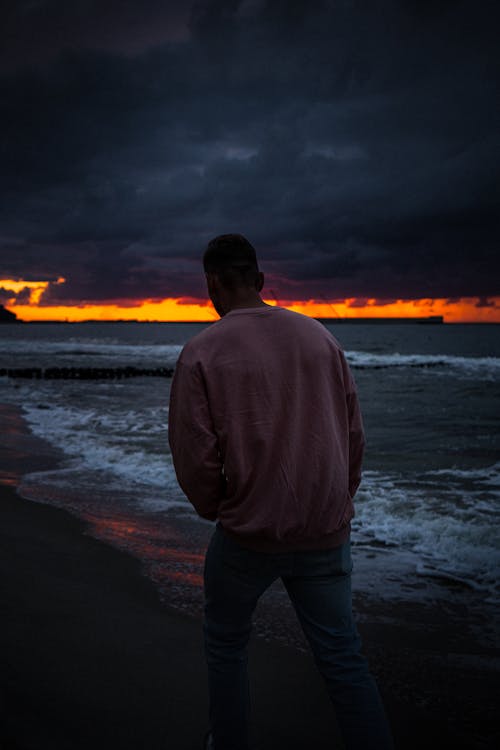 Free Back View of a Man in a Pink Sweater Walking at the Beach Stock Photo
