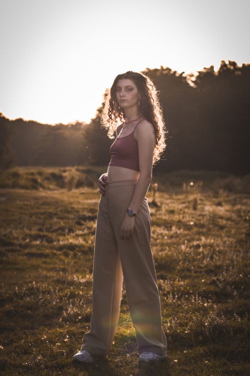 Free A woman in a crop top and pants stands outdoors, framed by a sunset glow. Stock Photo