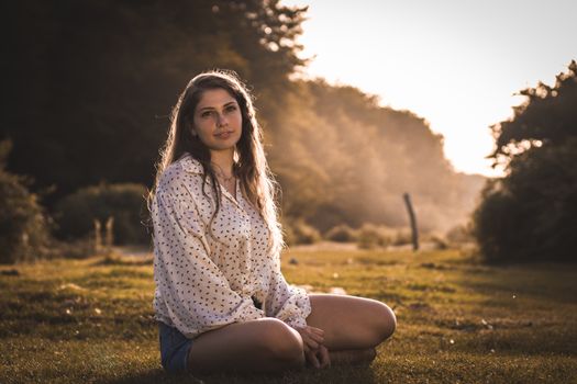 A serene moment of a woman sitting outdoors in a sunlit meadow during sunset.