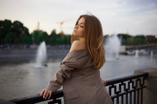 Woman Posing in a Beige Jacket with Bare Arm and Fountains in Background