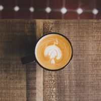 Latte art in a cup on a rustic wooden table — photo by SpotwizardLee on Pexels