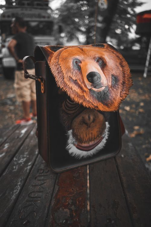 Free Artistic leather bag with bear design resting on wooden table outdoors, blending nature and craftsmanship. Stock Photo
