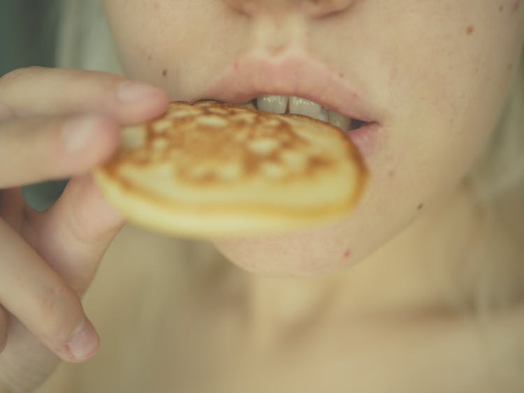 Person Eating A Small Brown Round Pancake

