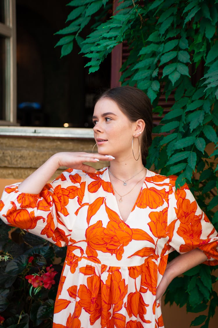 Portrait Of A Woman In Orange Pattern Dress Posing By A Window And Tree