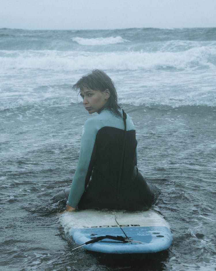 Woman In Wetsuit Sitting On The Surfboard