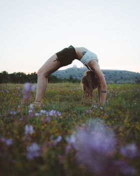 A woman practices yoga, doing a bridge pose in a field of flowers during sunset.