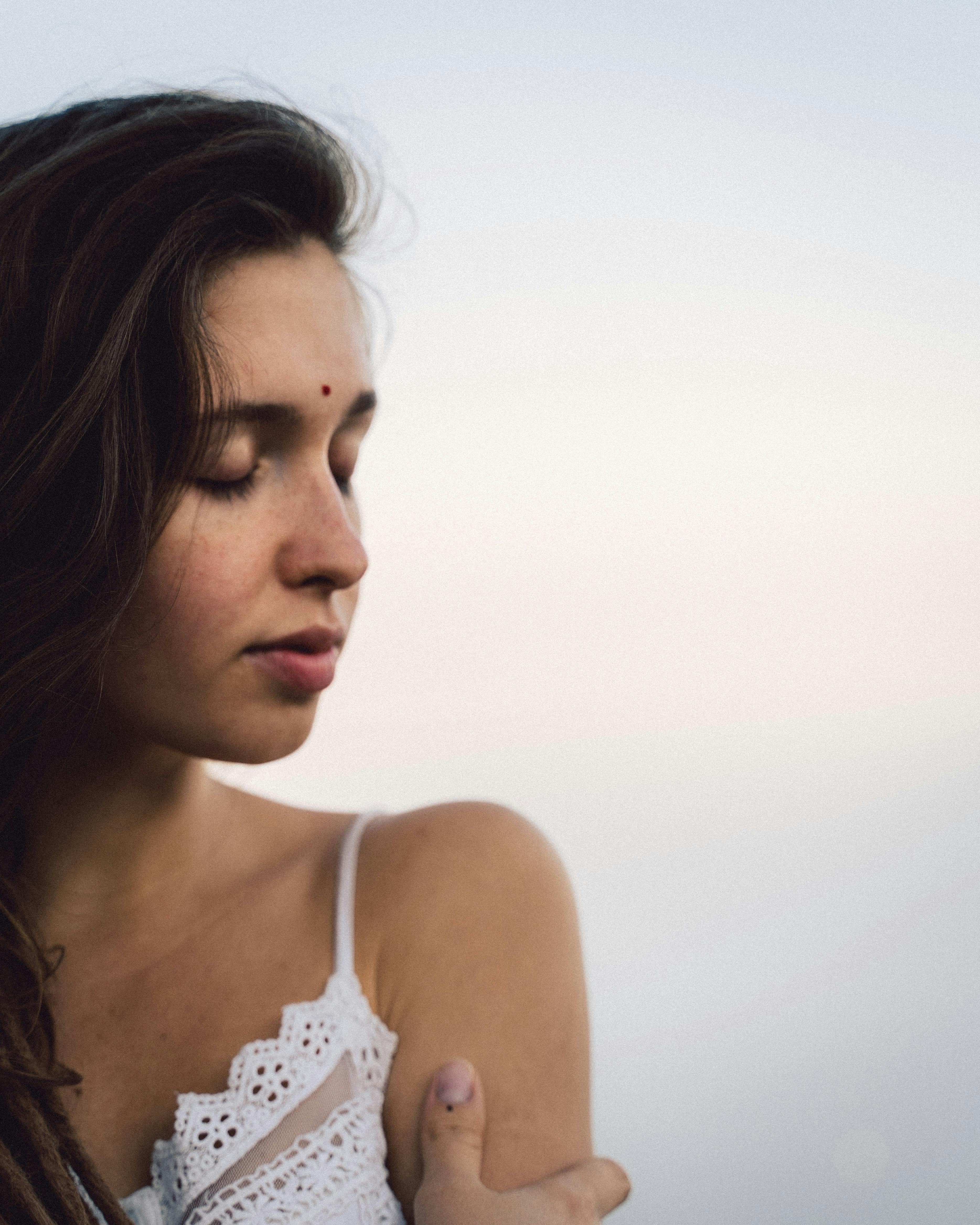 Close-up portrait of a young woman in a white lace top with eyes closed, exuding tranquility and beauty.