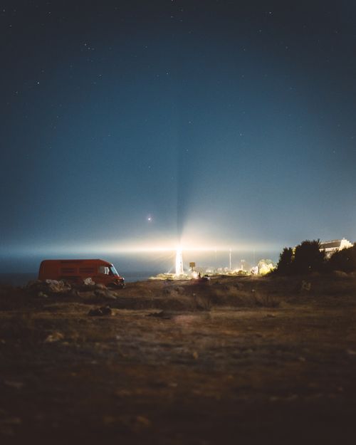 Free Scenic view of a bright lighthouse at night beside a red van with starry sky Stock Photo