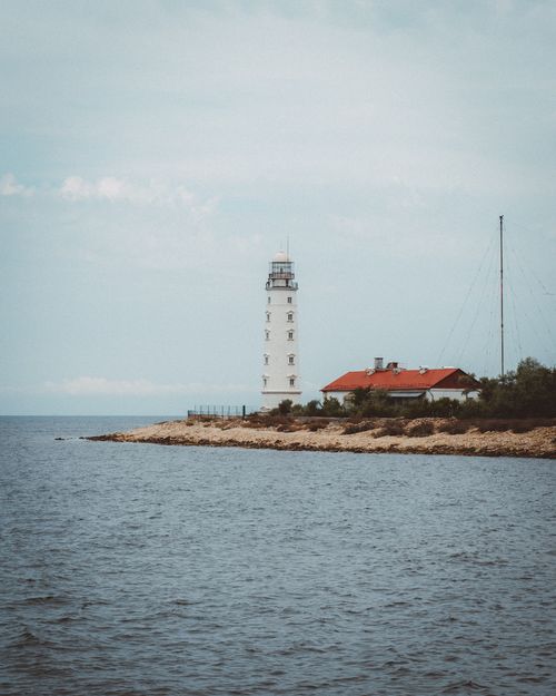 Free A tranquil view of a lighthouse by the rocky shore under a cloudy sky. Stock Photo