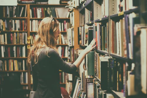 Free Woman in Black Long-sleeved Looking for Books in Library Stock Photo