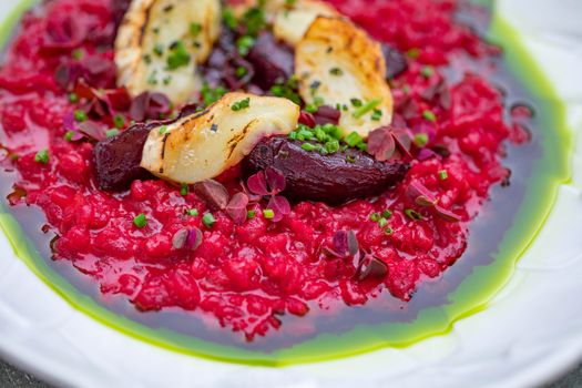 A colorful beetroot risotto topped with grilled halloumi and fresh herbs on a white plate.