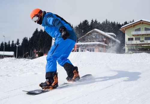 Free Snowboarder in vibrant gear carving through snowy slopes near a ski resort on a bright winter day. Stock Photo