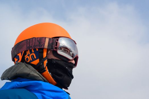 Close-up of a man wearing winter sports gear and reflective goggles against a cloudy sky.