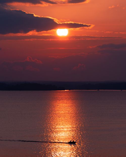 Free A breathtaking sunset view over the ocean with a small boat silhouette enhancing the tranquility. Stock Photo