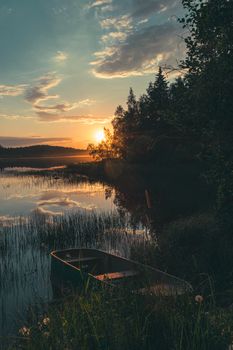 Tranquil sunrise scene with a wooden boat on a calm lake, surrounded by nature.