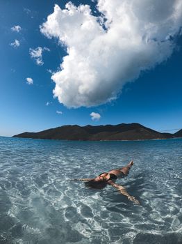A woman floating in clear ocean waters under a blue sky in Arraial do Cabo, Brazil.