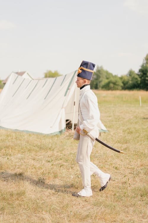 Man in French Napoleonic Forage Cap and Uniform Walking Through the Camp with a Saber at His Side
