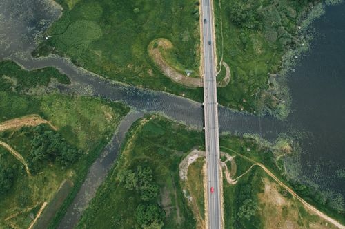 Free Aerial view of a road bridge crossing lush green fields and a winding river. Stock Photo