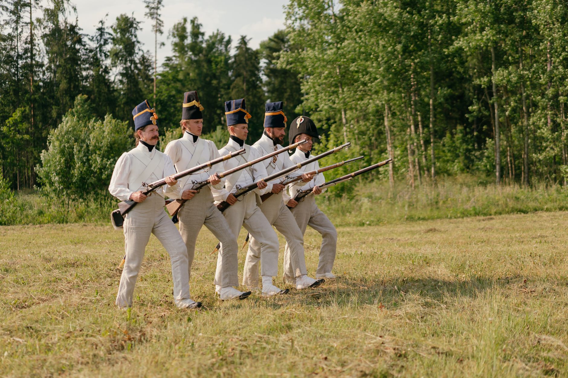 Soldiers in historical uniforms marching during a reenactment in nature.