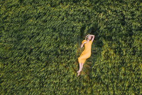 Free Aerial shot of a woman in a yellow dress relaxing in a lush green field, exuding tranquility. Stock Photo